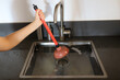 Overflowing kitchen sink, clogged drain. Hand holding plunger (force cup). Plumbing problems.