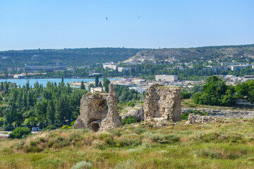 Wall Mural - Panorama of medieval towers of Kalamita, fortress founded by Byzantines. It was built above cliff hiding cave church of St Clement. Modern city Inkerman (Crimea) and Sevastopol bay are on background