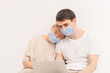 © TT - A family in medical masks look at a laptop. The old mother and young son. The concept of self-isolation at home due to the virus pandemic. Spending time during quarantine.