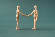 Two Wooden Figures Shaking Hands On Blue Background, Friendship Or Agreement Concept