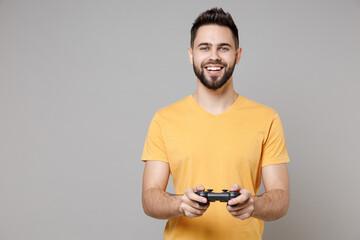 Wall Mural - Young caucasian smiling bearded student gamer happy cheerful fun man 20s wearing casual yellow basic t-shirt playing pc game with joystick console isolated on grey color background studio portrait.