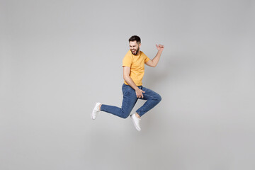 Wall Mural - Full length of young bearded student smiling happy overjoyed man 20s in yellow basic t-shirt jump high playing guitar gesture flying outstretched hands isolated on grey background studio portrait
