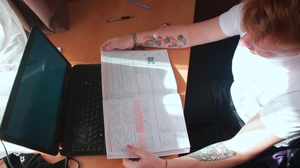 Poster - Examining a printed outline at the table. The student prepares for the lesson online. Transfer of knowledge using high-speed Internet.