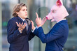 © VISTA by Westend61 - Male professional in pig mask pointing coworker while holding collar by glass wall