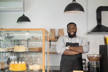 Smiling and friendly African-American small business owner, cafe manager, multiracial bakery waiter stands behind the counter in confident pose with arms crossed and looks at the camera