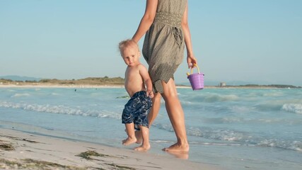 cute child looking around at seashore. baby boy walking with mother at beach.