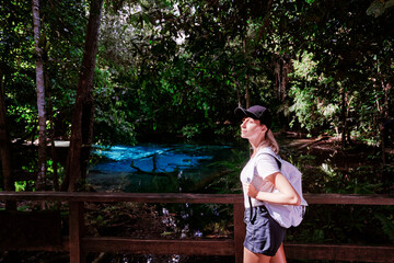 Wall Mural - Young woman in hat with rucksack enjoying view of amazing crystal clear emerald pool in mangrove forest, Krabi, Thailand.