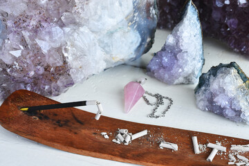 Wall Mural - A close up image of burning incense stick with several amethyst crystals on a white table top. 