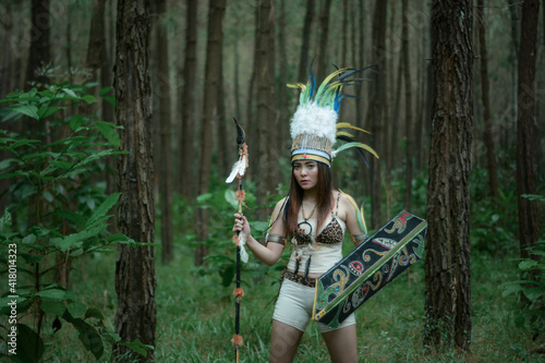 Plakat Portrait of young girl in costume native American Indian holding spear and shield in forest