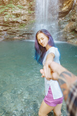 Canvas Print - Young woman holding man's hand and leading him to waterfall, point of view. Focus on face.