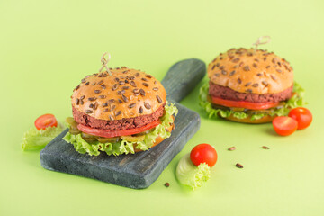 Two vegan burgers with beetroot patty on a wooden serving board on a bright green background. Fast food for a meat-free diet.