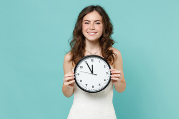 Wall Mural - Smiling cheerful bride young woman 20s years old in beautiful white wedding dress hold in hand clock isolated on blue turquoise color background studio portrait. Ceremony celebration party concept.