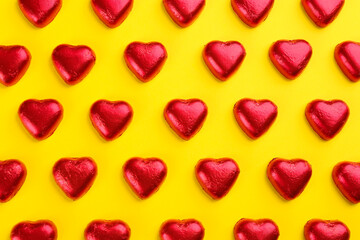 Wall Mural - Heart shaped chocolate candies in red foil on yellow background, flat lay