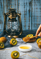 Sticker - Vertical shot of a hand holding a wooden dipper with honey surrounded by kiwis next to a lantern