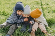 © Ananass - three children, 2 boys and a girl sitting on the green grass dressed in warm spring clothes. Brothers and sister have fun on a walk