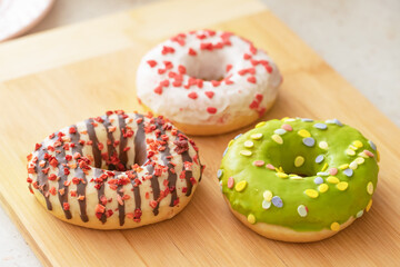 Confectionery product. Donut decorated with colored icing. Three donuts are on a brown wooden board.