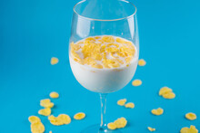 Milk In A Glass And Scattered Yellow Corn Flakes On A Blue Background