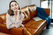 © rh2010 - Portrait of beautiful woman smiling and looking at camera while sitting on brown comfortable sofa on home interior background. Lifestyle and home coziness concept.