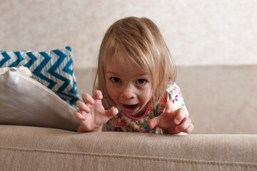 A little beautiful girl lies on the couch and looks into the camera