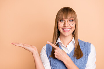 Poster - Photo portrait of happy girl in spectacles showing pointing copyspace on hand isolated on pastel beige color background