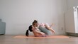 Mother lies on yoga mat and kiss her little baby on her legs