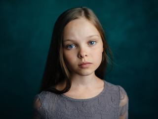 cute blue-eyed girl in a gray dress on a green background cropped view