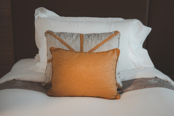 Bed with clean white pillows and scatter cushion in hotel room.