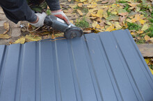 A Man Is Cutting A Corrugated Metal Sheet, Steel Roof Or Siding Panel With An Angle Grinder.