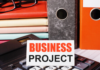 Fototapete - Next to the diaries and folders with documents on the calculator there is a white card with the inscription BUSINESS PROJECT