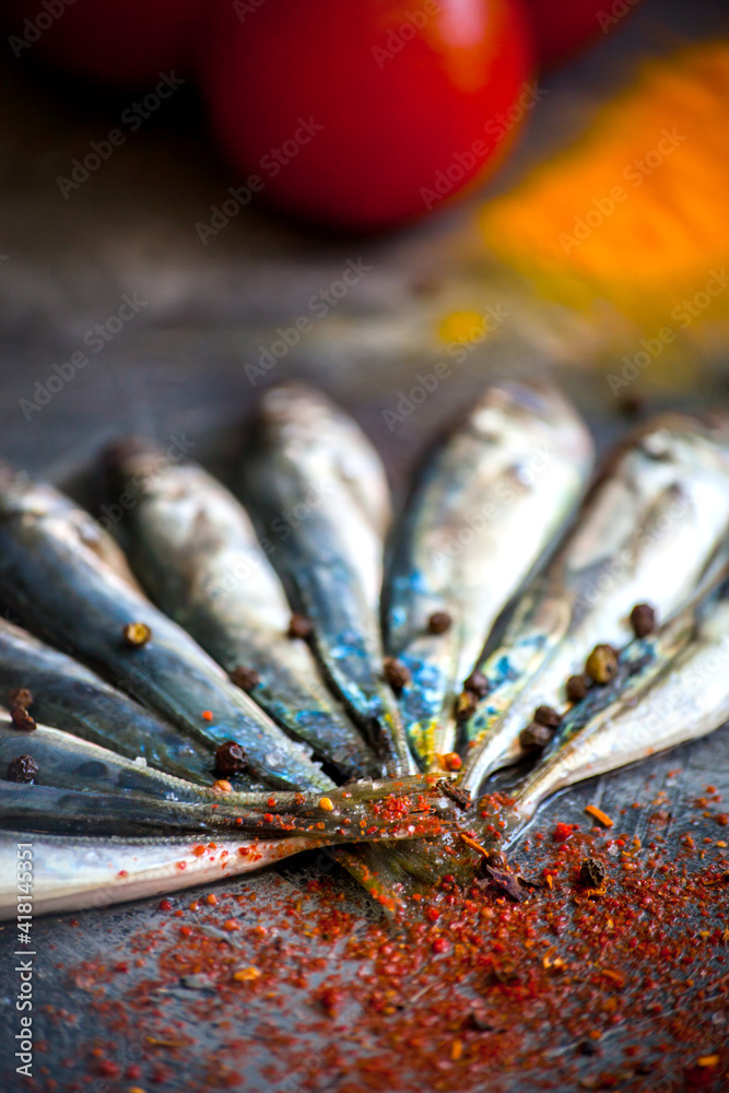 Small fresh sea fish lies on a dark background with bright spices - obrazy, fototapety, plakaty 
