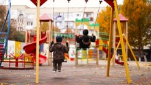 Ride Fast On The Baby Swing. Children Ride A Swing In The Playground. Boys 8 10 Years Old In Warm Clothes Are Walking In The City Park