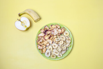 Wall Mural - dried apples and bananas on a plate and fresh apple and banana on a yellow background