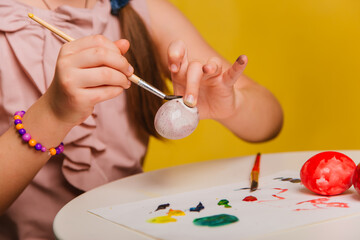 A girl in a pink dress paints eggs for the religious holiday of Easter. The child draws on eggs.