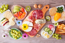 Spring Or Easter Theme Charcuterie Table Scene Against A Wood Background. Variety Of Cheese, Meat, Fruit And Vegetable Appetizers. Top View.