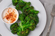 Close-Up Top View of Grilled Broccoli on a White Plate with Paprika-Topped Sauce on Gray Background.