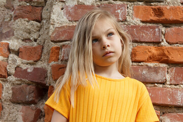 Beautiful little five-year-old girl with blond hair in yellow clothes on the background of an old brick wall.