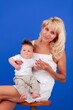 © fibeelf - Mother with a little son in her arms in white clothes sits on a stool on a blue