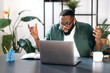 © Kateryna - Dissatisfied confused multiracial black guy, male freelancer or manager, discouraged looks at the laptop, received unexpected message or news, sitting at workplace