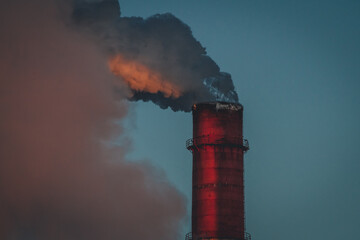 thick smoke from fuel combustion is pouring into the atmosphere from a huge chimney of a thermal power plant