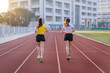 © EduLife Photos - Two young Asian women in sports outfits jogging on running track in city stadium in the sunny morning to keep fitness and healthy lifestyle. Young fitness women run on the stadium track