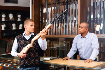 Two serious men choosing pneumatic weapon in military store