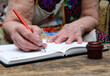 An elderly woman holds a fountain pen in her hand. She writes down the expenses in her diary. Next to it is a vintage inkwell. Concept-economy, housekeeping