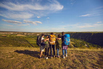 Wall Mural - group of hikers with backpacks standing on mountain top and observing scenery, back view. young frie