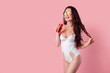 © ZaStock - Excited young woman girl in white one-piece swimsuit, sunglasses posing with beverage isolated on pink background. People summer vacation rest lifestyle concept.