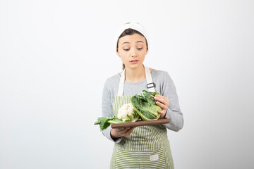 Wall Mural - Photo of a young woman in apron holding a wooden plate with cauliflowers