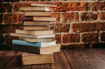 Poster - Stack of books in the library room lay on the wood table with brick backround.