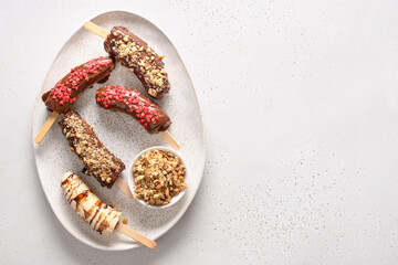 Banana lollipops with walnuts and red hearts sprinkles in plate on white background. Homemade sweets. View from above. Copy space.