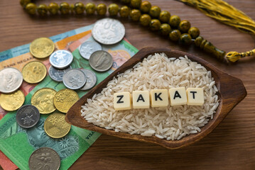 Concept of zakat in Islam religion. Selective focus of money, rosary beads and rice with alphabet of zakat on wooden background.