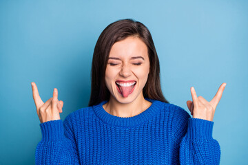 Wall Mural - Portrait of young happy crazy excited positive girl stick tongue out showing rock n roll sign isolated on blue color background