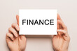 © Daria Lukoiko - Female hands hold card paper with text FINANCE on a yellow background. Business and finance concept